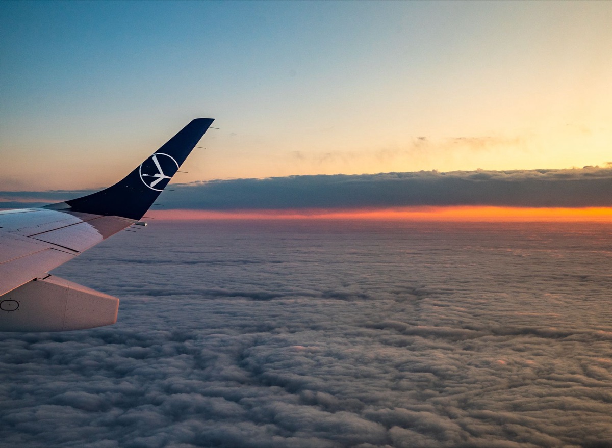 Vista de uma asa de avião voando sobre as nuvens ao pôr do sol